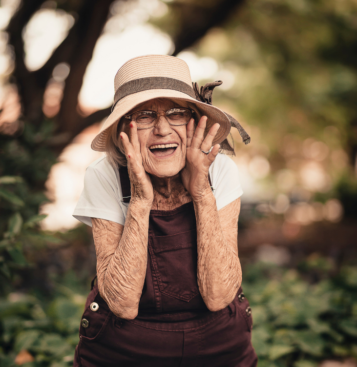 Elderly lady holding hands to either side of mouth laughing.