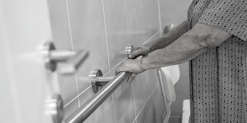 Close up of an elderly person holding onto a grab rail with both hands.