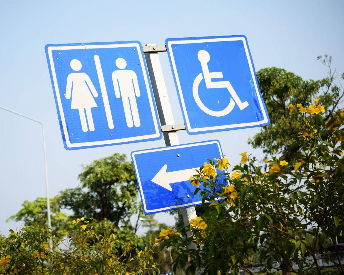 Signage of unisex toilet, international symbol for access and arrow pointing to the left.